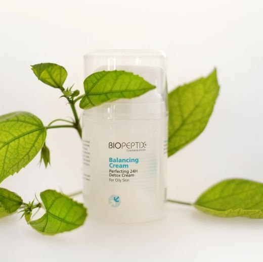 A bottle of biopeptix balancing cream surrounded by green leaves