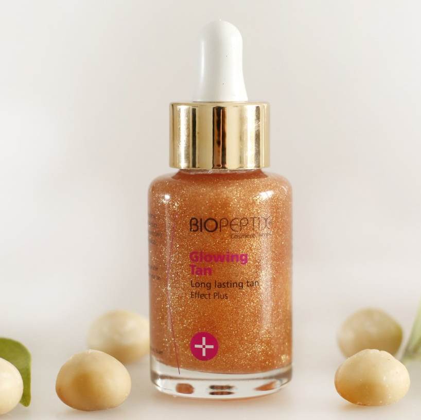 A bottle of biopeptix glowing tan next to macadamia nuts