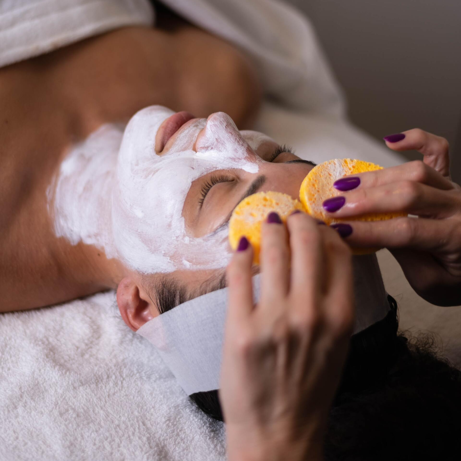 A woman with purple nails is getting a facial treatment