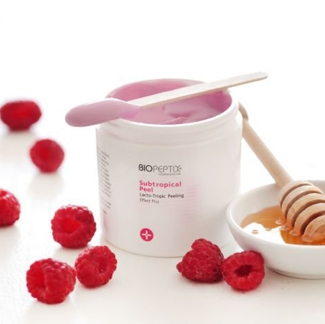 A jar of biopeptide subtropical peeling next to raspberries and honey