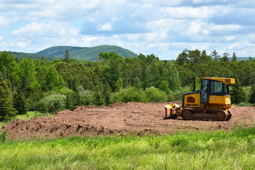 Yellow bulldozer clearing a dirt field with trees and hills in the background