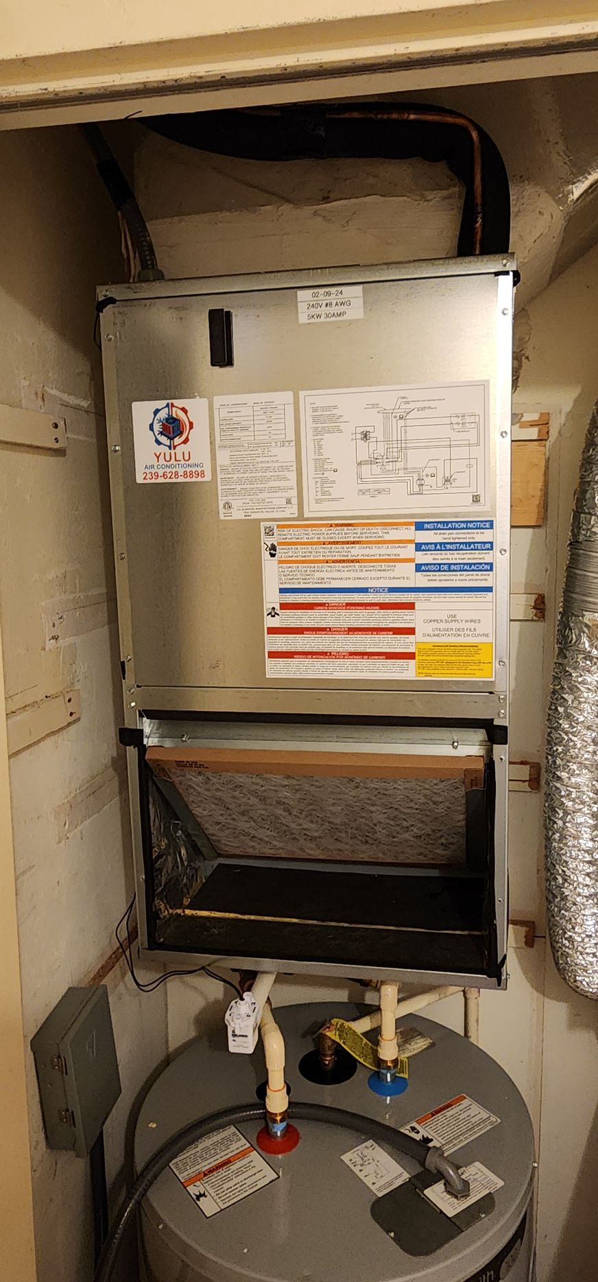A water heater is sitting next to an air conditioner in a closet.