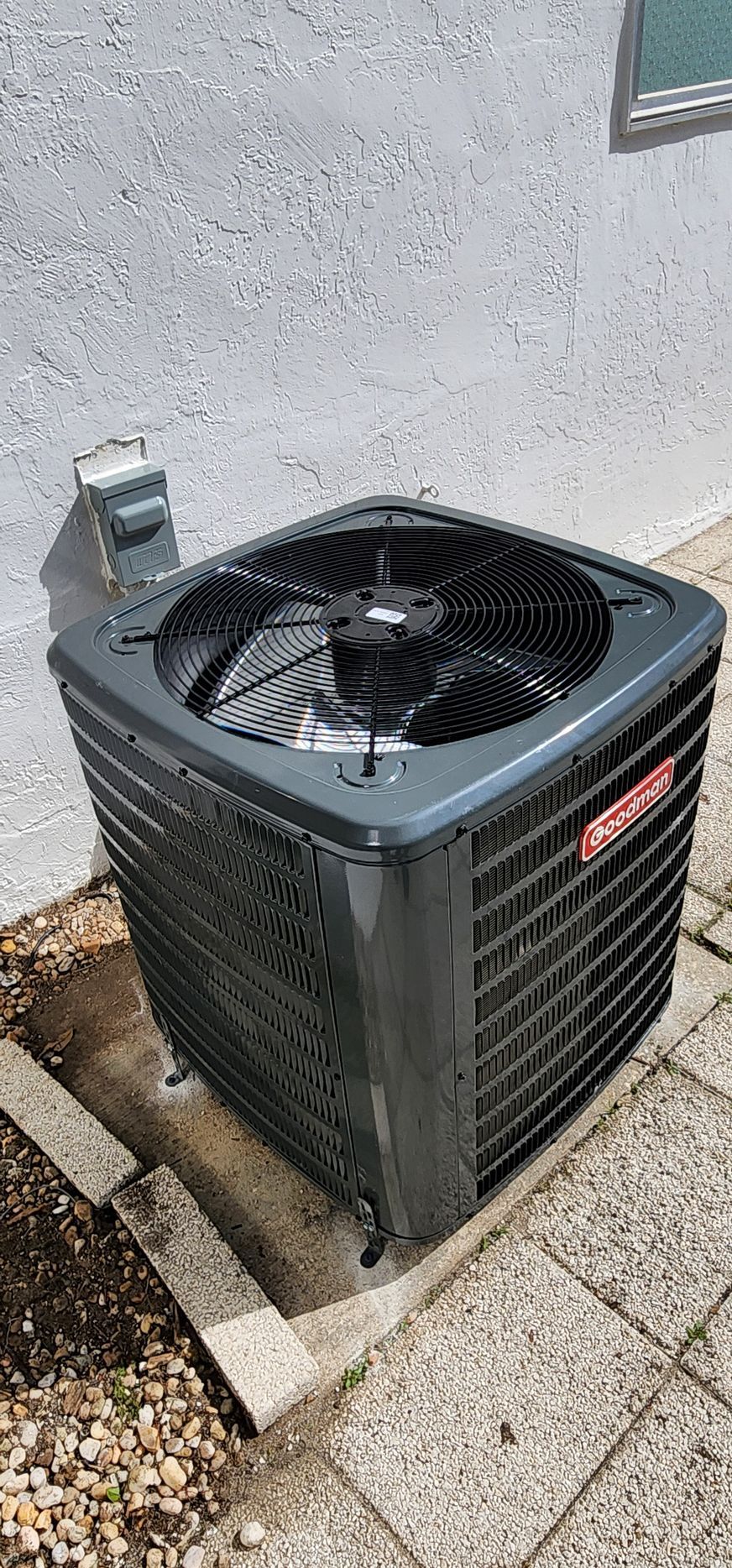 A black air conditioner is sitting on a sidewalk next to a wall.