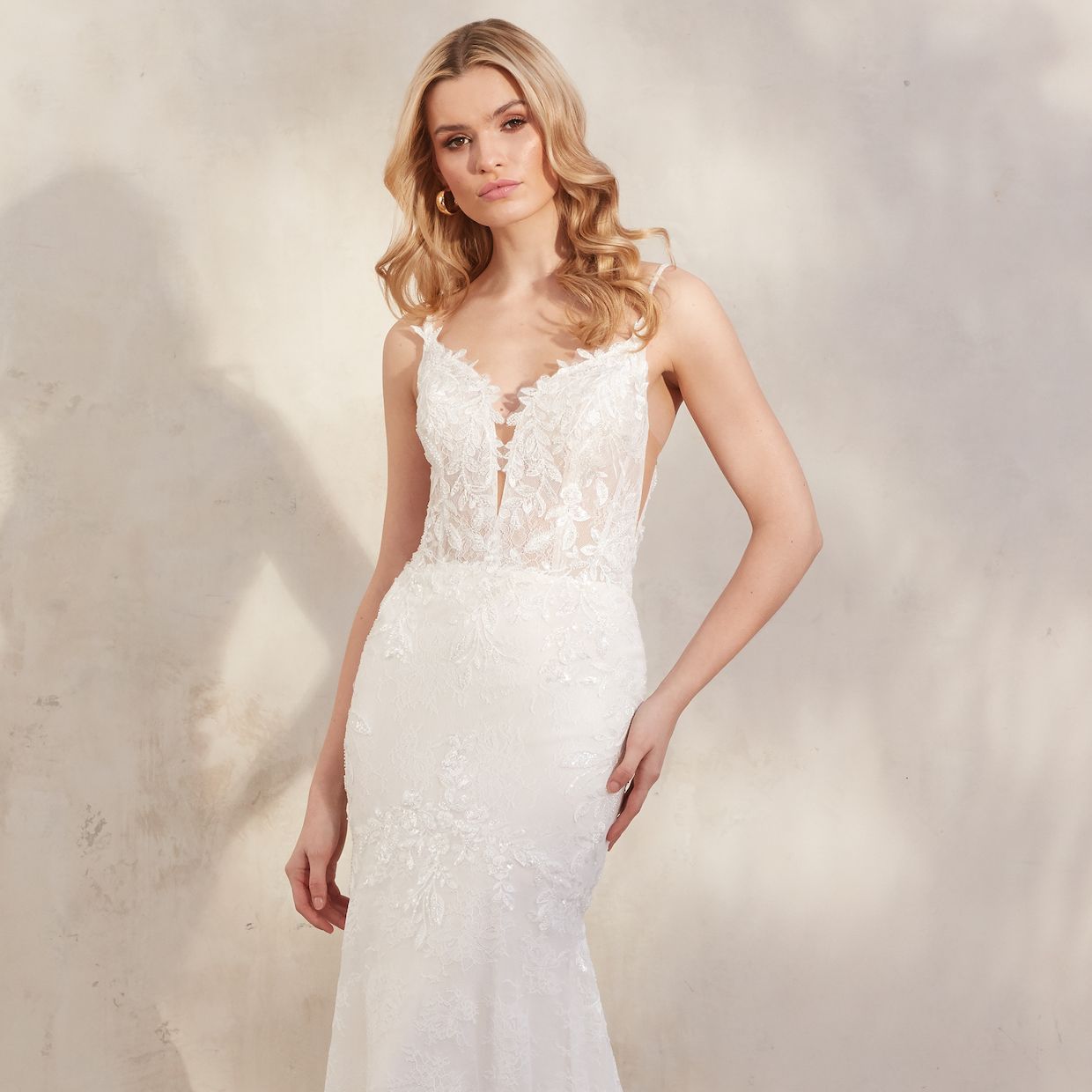 Woman in a white lace gown posing against a soft beige studio backdrop