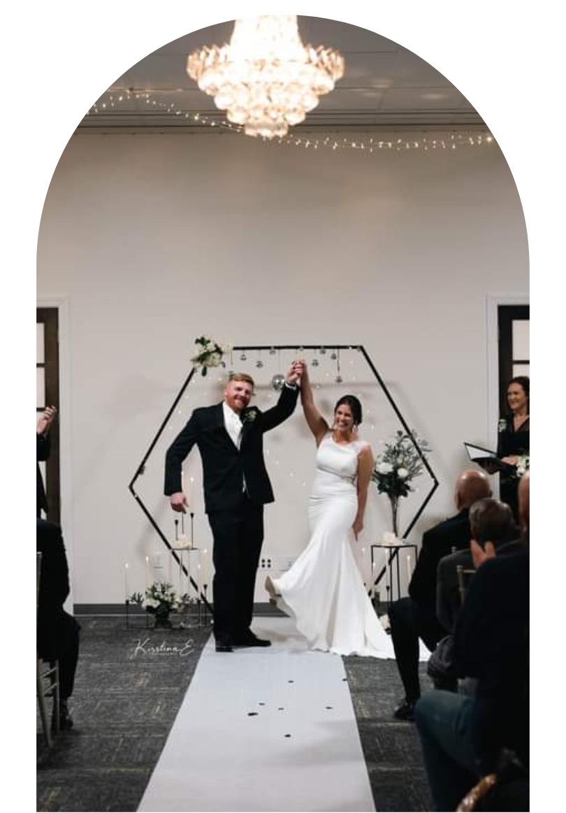 Newlyweds walking down the aisle, hand in hand, in a white-walled ceremony hall