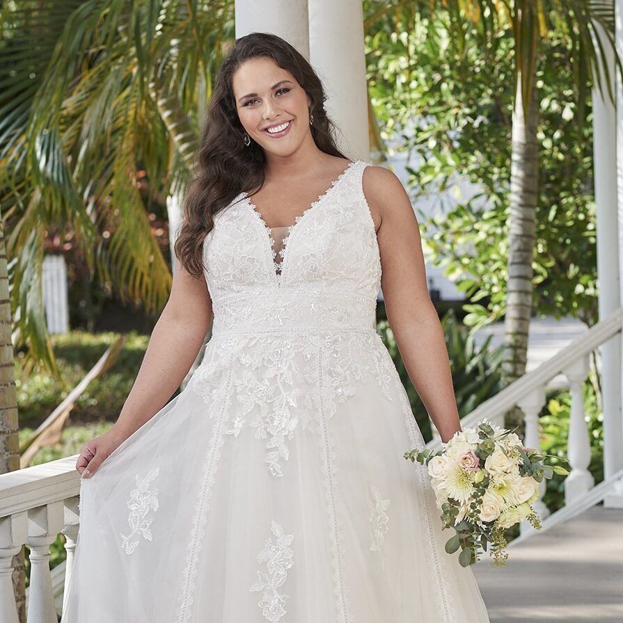 Bride in a white lace wedding dress holding a bouquet on a garden walkway