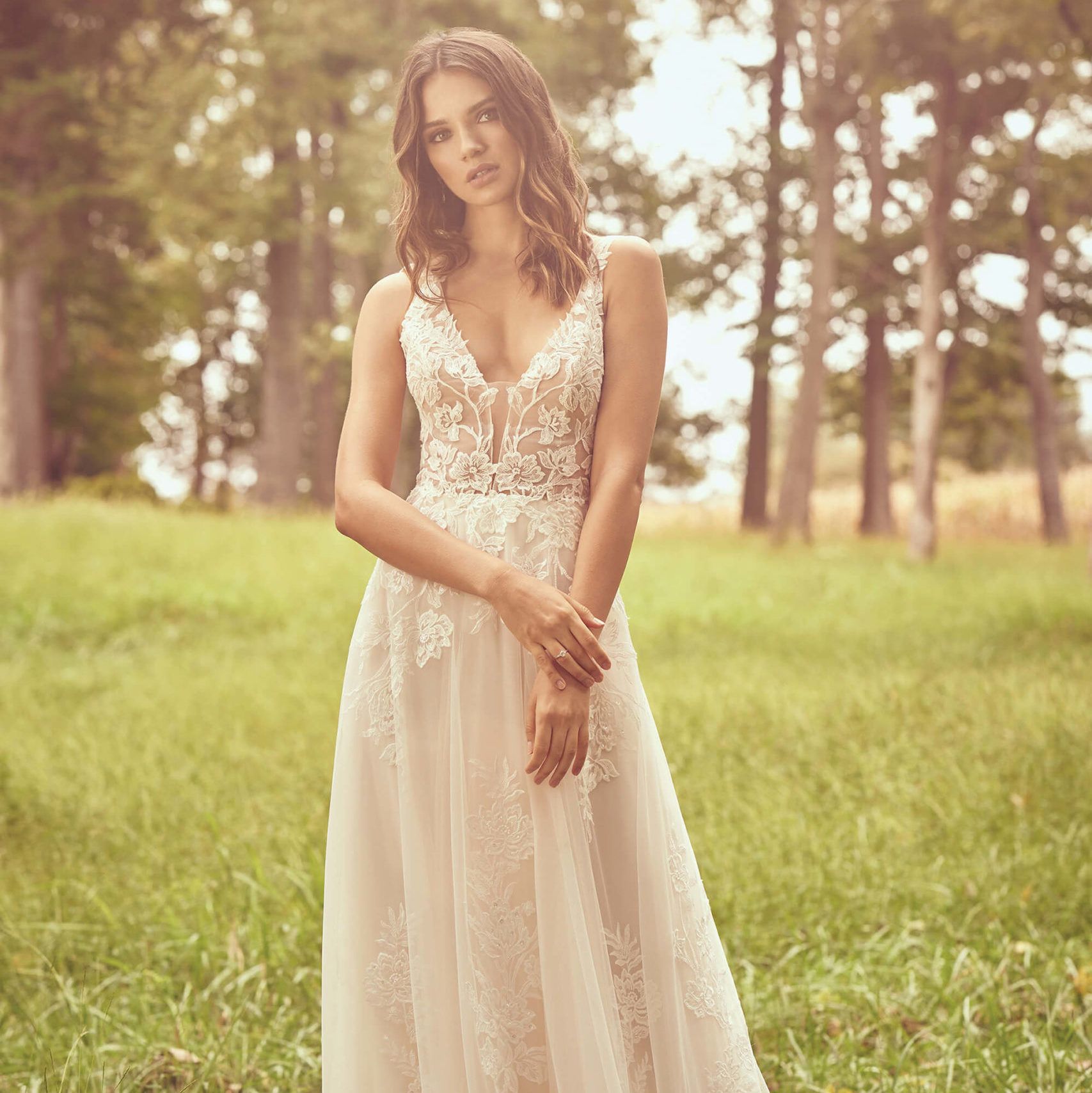 Woman in a white lace dress standing in a grassy field with trees in the background