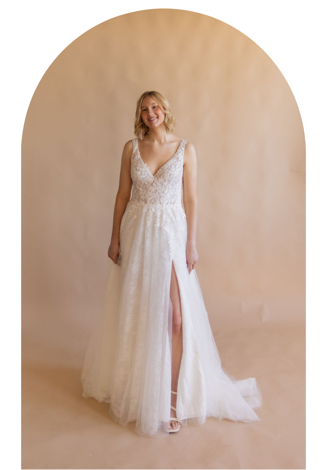 Bride in a white lace wedding gown standing before a soft beige backdrop