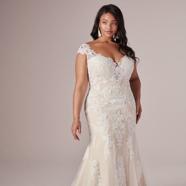 Woman in a cream lace wedding gown posing against a neutral backdrop