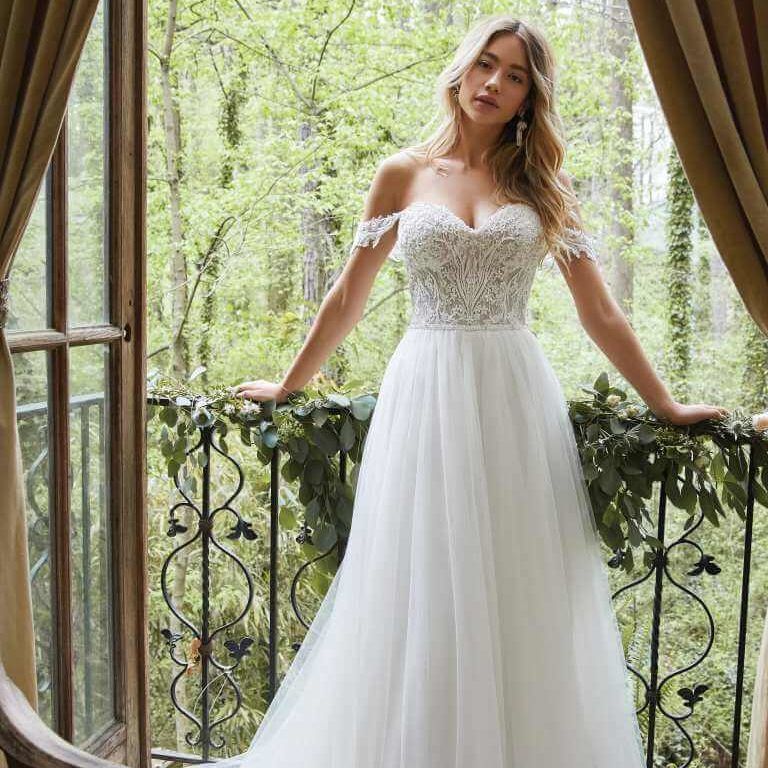 Woman in a white lace dress standing on a balcony overlooking a lush green forest