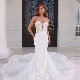 Woman in a white lace wedding gown with a long train, standing on a porch before ornate double doors