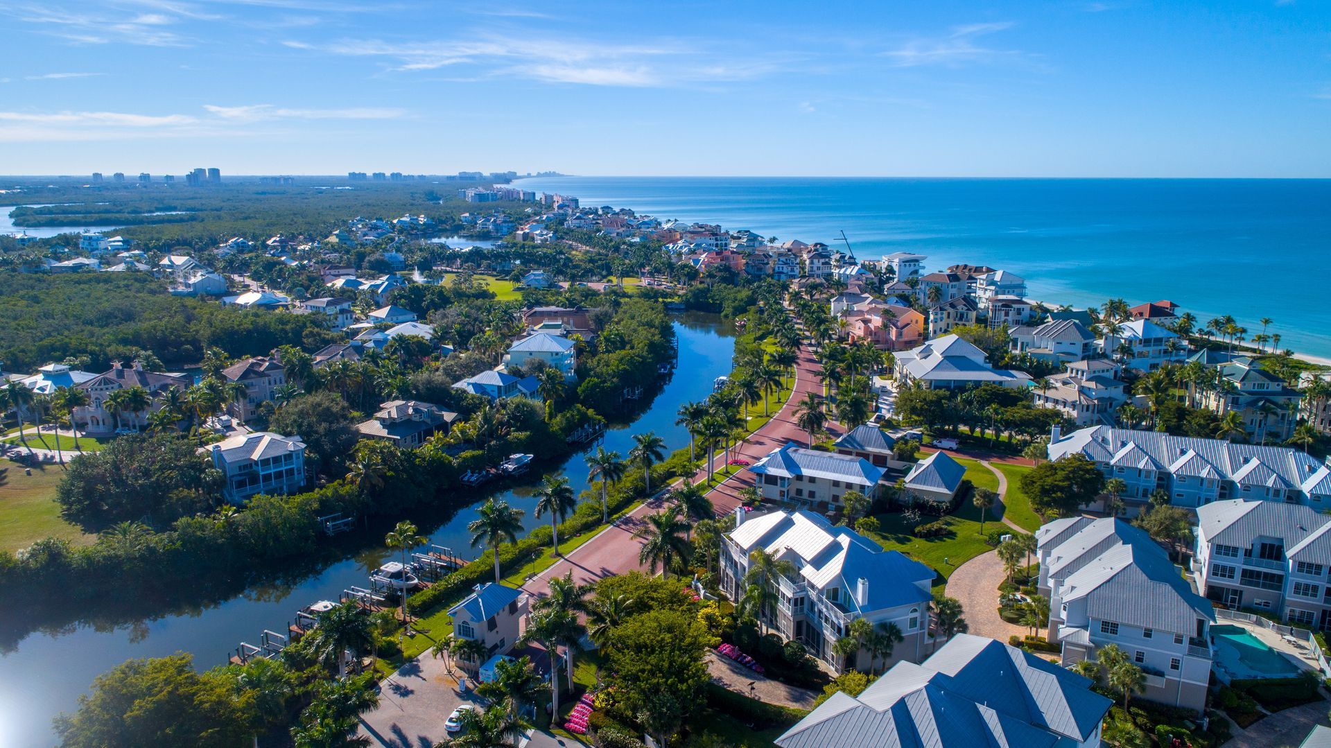 An aerial view of a coastal neighborhood with houses nestled along a winding river, leading to the blue ocean.