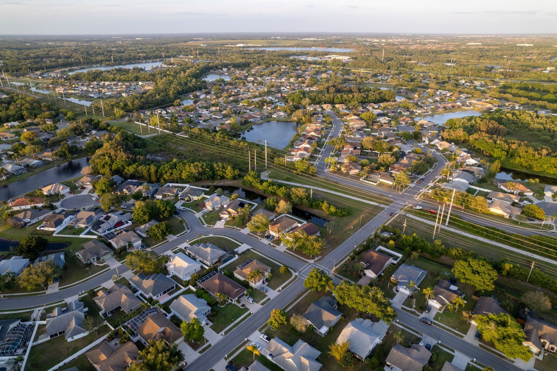Aerial view of suburban homes, streets, and trees near a lake.