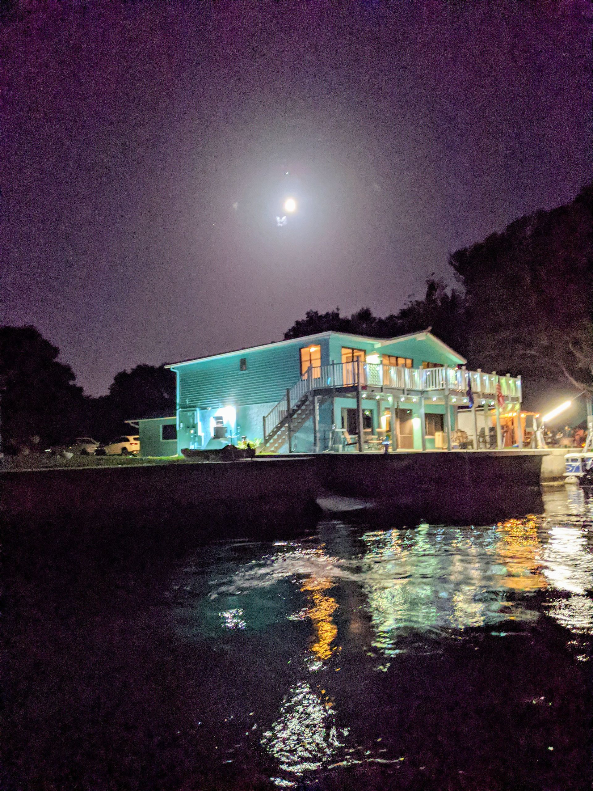 A house is lit up at night with a full moon in the sky