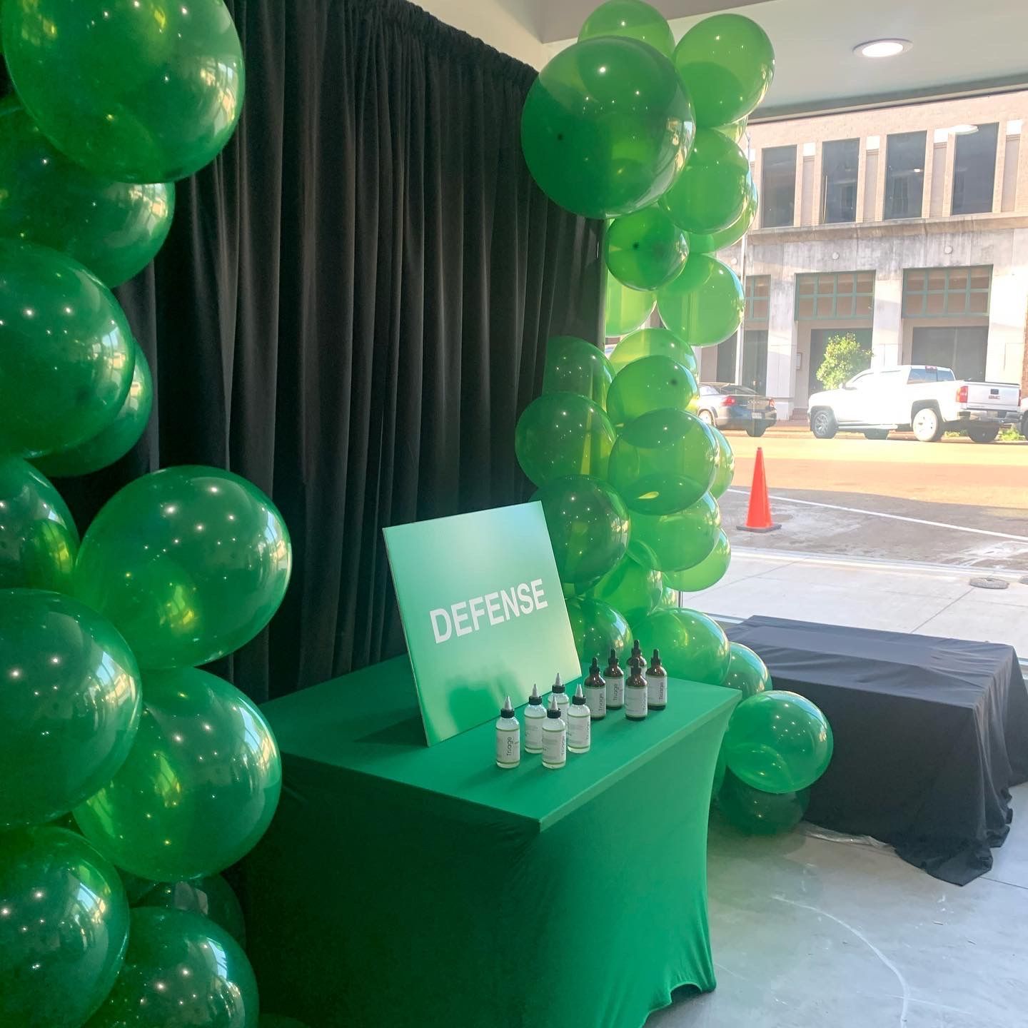 Green balloon-decorated event table with a “DECFEST” sign and drink bottles by a window on a rainy street