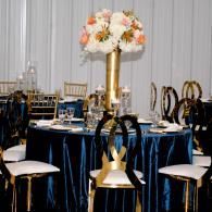 Elegant banquet table with navy linens, gold chairs, and a tall white-and-peach floral centerpiece