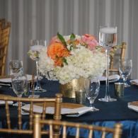 Elegant banquet table with navy linens, gold chairs, and a white-and-orange floral centerpiece