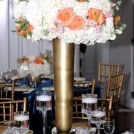 Floral centerpiece with white and peach flowers on a gold pedestal at a decorated table setting