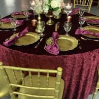Formal dining table set with purple decor, gold chargers, and floral centerpiece