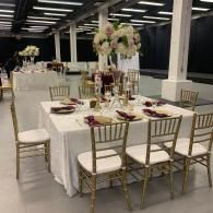 Elegant banquet table set with white linens, gold chairs, and floral centerpiece in a bright indoor venue