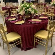 Round banquet table with burgundy tablecloth, gold chairs, and floral centerpiece at an event venue