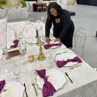 Woman arranging purple napkins on a decorated banquet table in a bright event hall