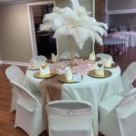 Round banquet table with white chair covers and a tall white feather centerpiece in a reception hall