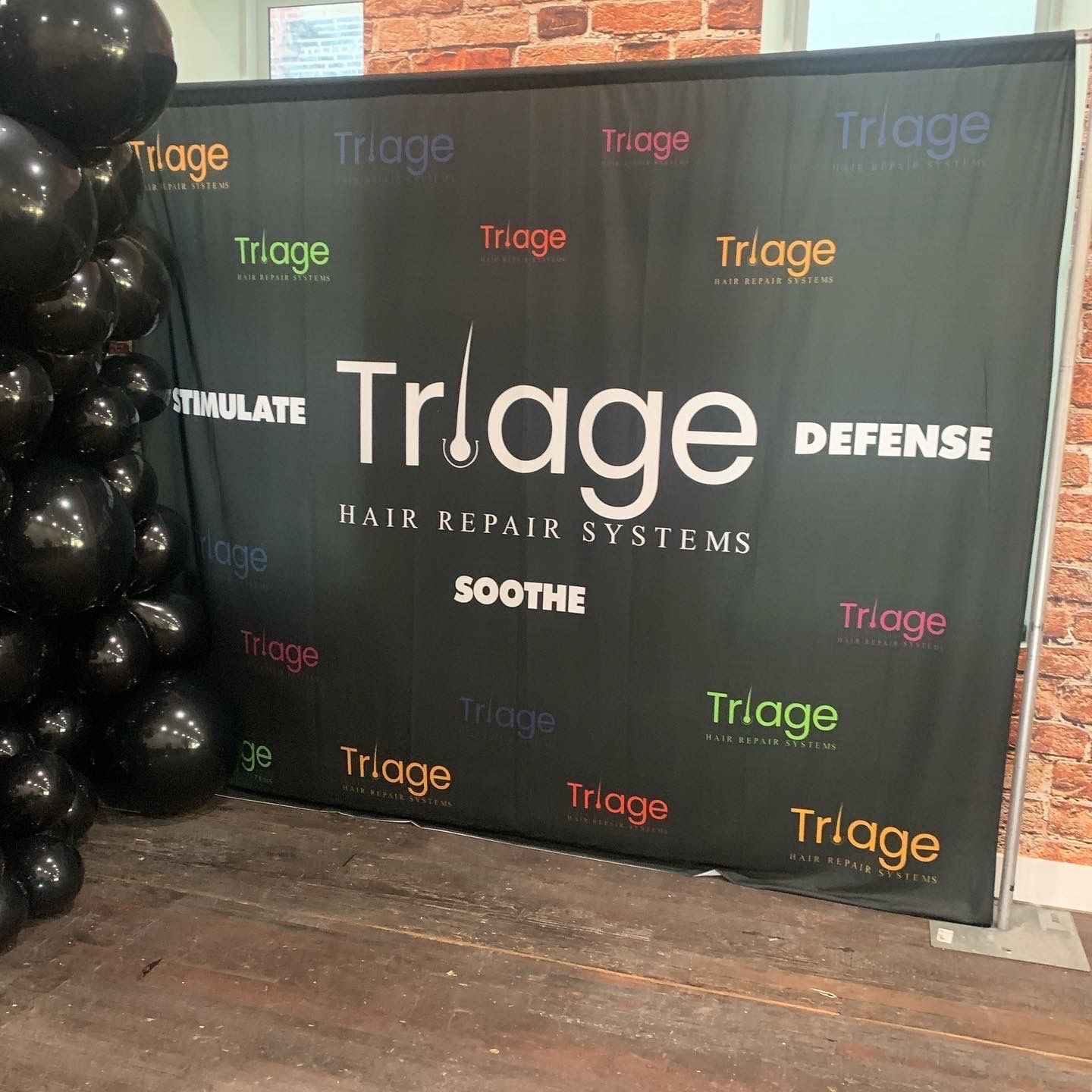 Triage Defense backdrop with black balloons on the left, on a wood floor
