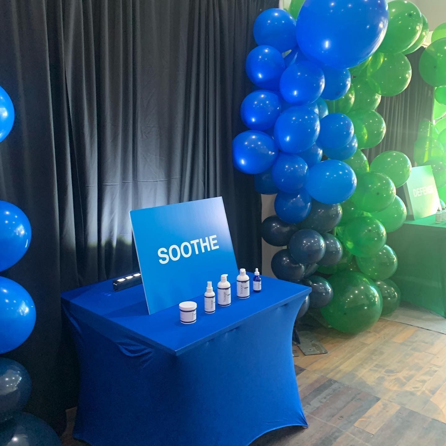 Blue SOOTHE product display table with bottles, beside green and blue balloon decorations