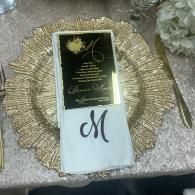 Gold-and-black invitation card with a white envelope monogrammed “M” on a textured decorative tray.