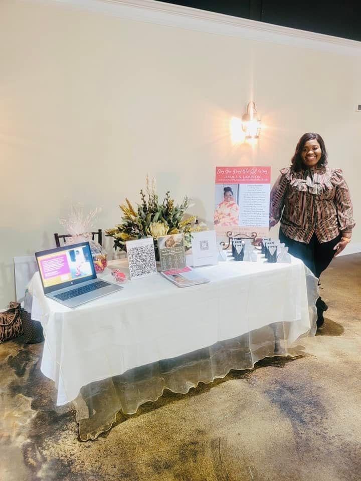 Display table with laptop, flowers, and signboards; a woman stands beside it in a softly lit room.