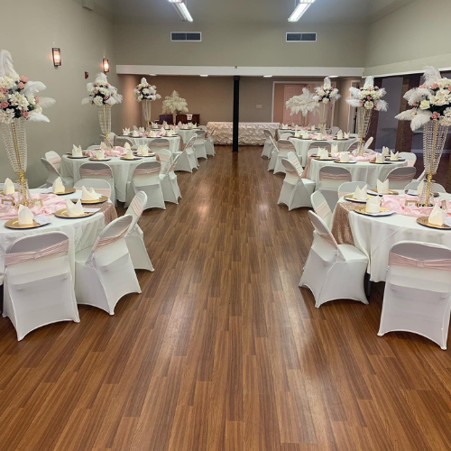 Decorated banquet hall with round tables, white chair covers, and floral centerpieces on a wood floor.