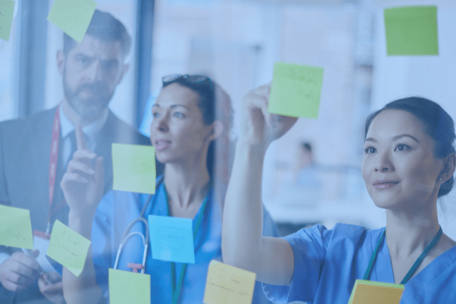 a group of doctors and nurses are putting sticky notes on a glass wall .