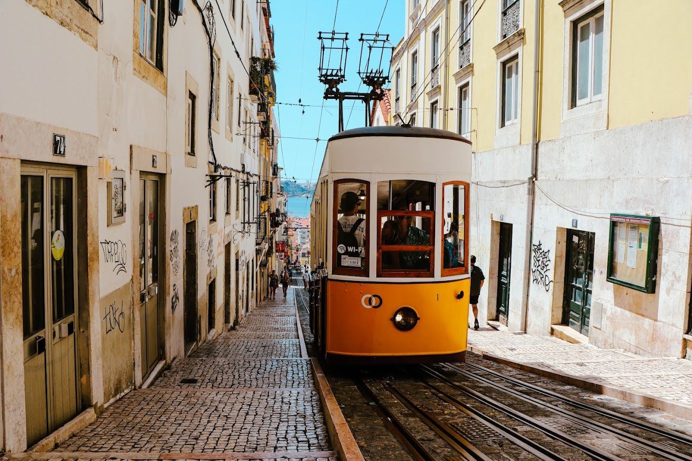 Yellow tram on a narrow cobblestone street between tall buildings in a historic city
