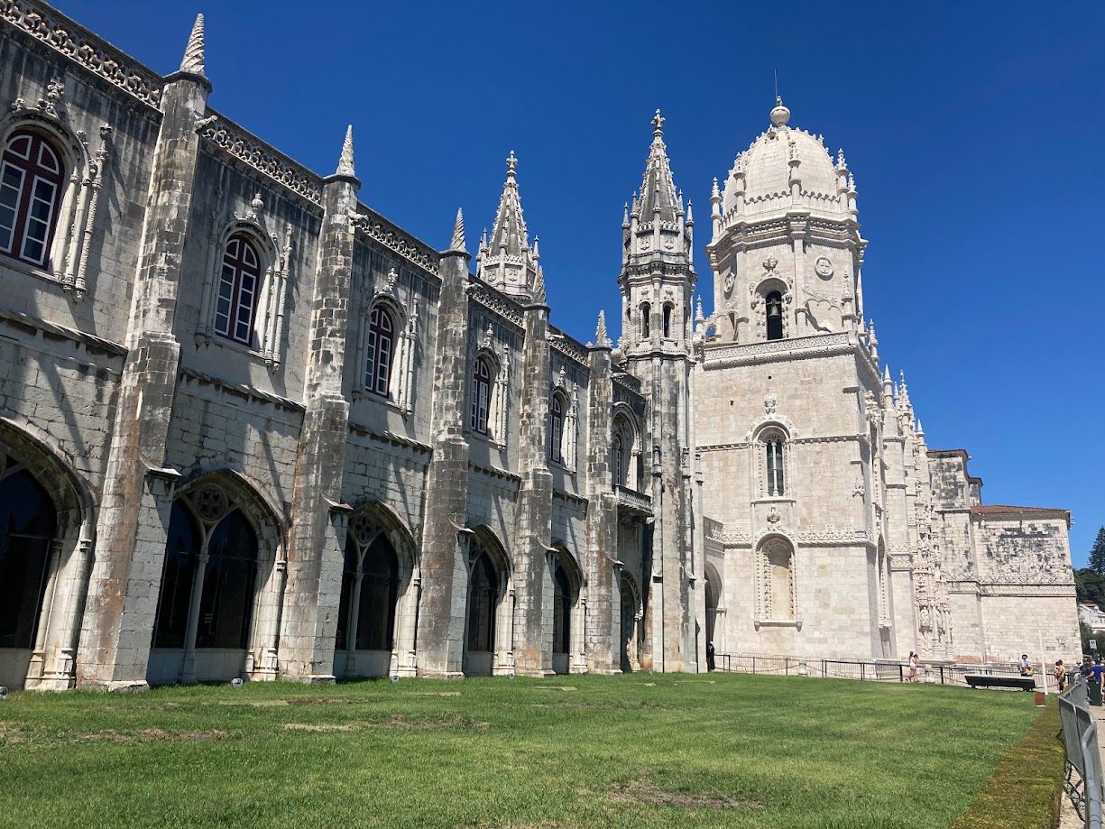 Stone cathedral with ornate towers and arches beside a green lawn under a clear blue sky