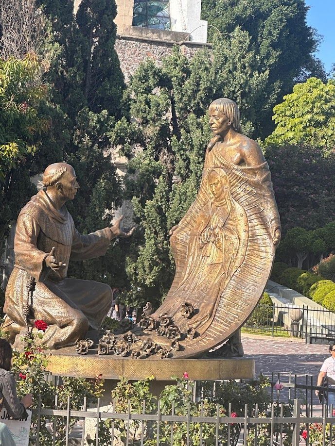 Bronze statues of two people conversing in a garden, with trees and a stone walkway behind them