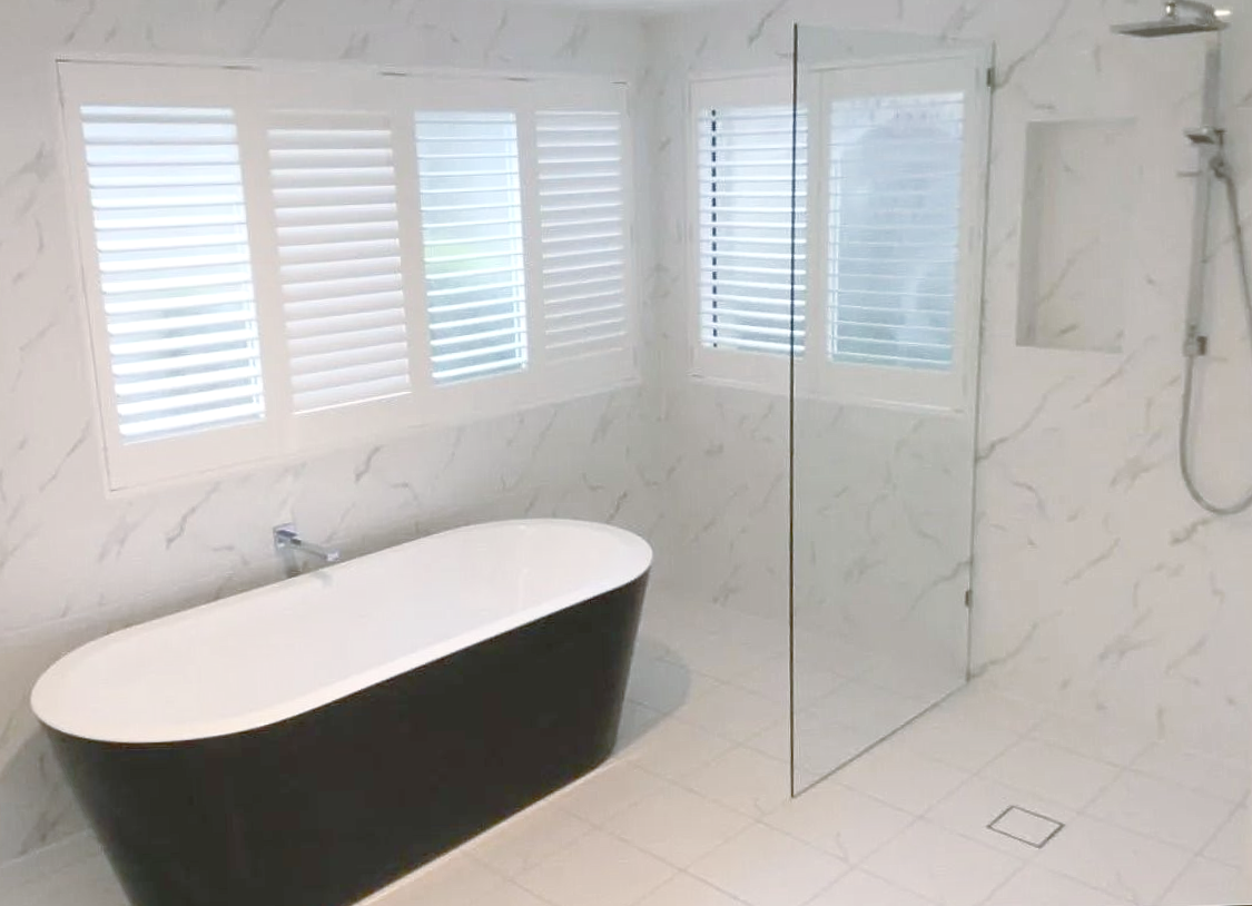 Bathroom with a black freestanding tub, white tile, and window shutters — Platinum Kitchens & Bathrooms in North Boambee Valley, NSW