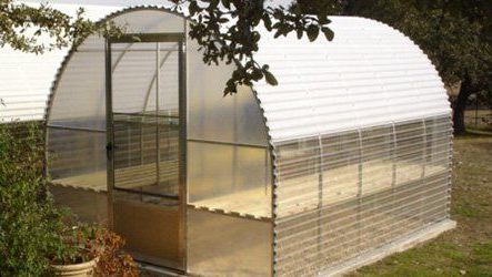 A greenhouse is sitting in the middle of a grassy field.