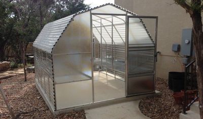 A greenhouse is sitting in the backyard of a house.