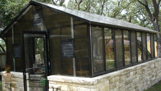 A greenhouse with a stone wall and trees in the background.