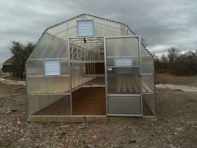 A greenhouse is sitting in the middle of a dirt field.
