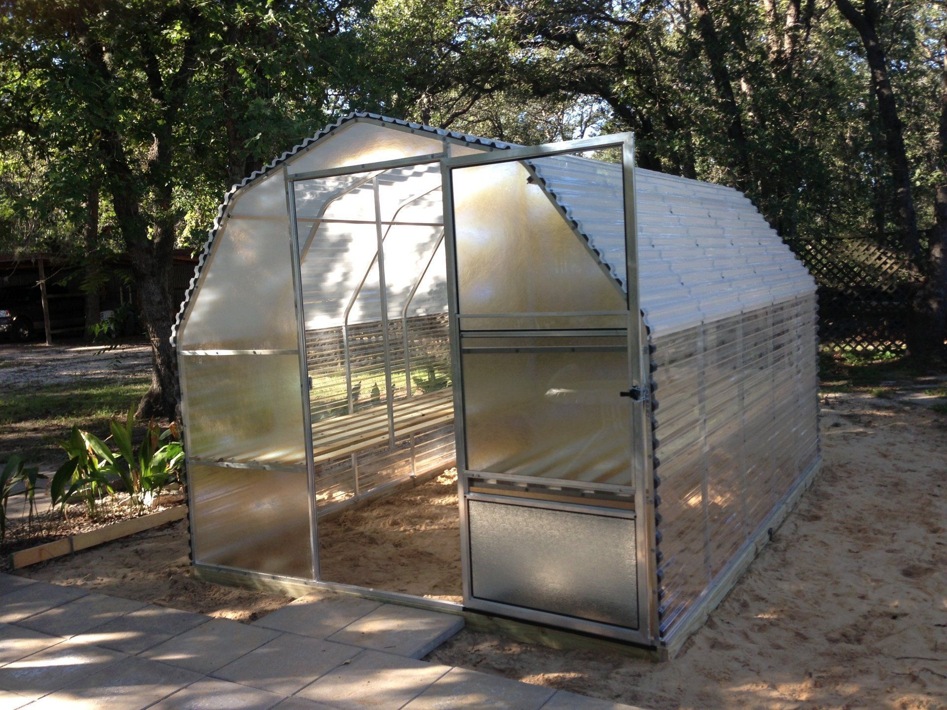 A greenhouse is sitting in the middle of a sandy area surrounded by trees.