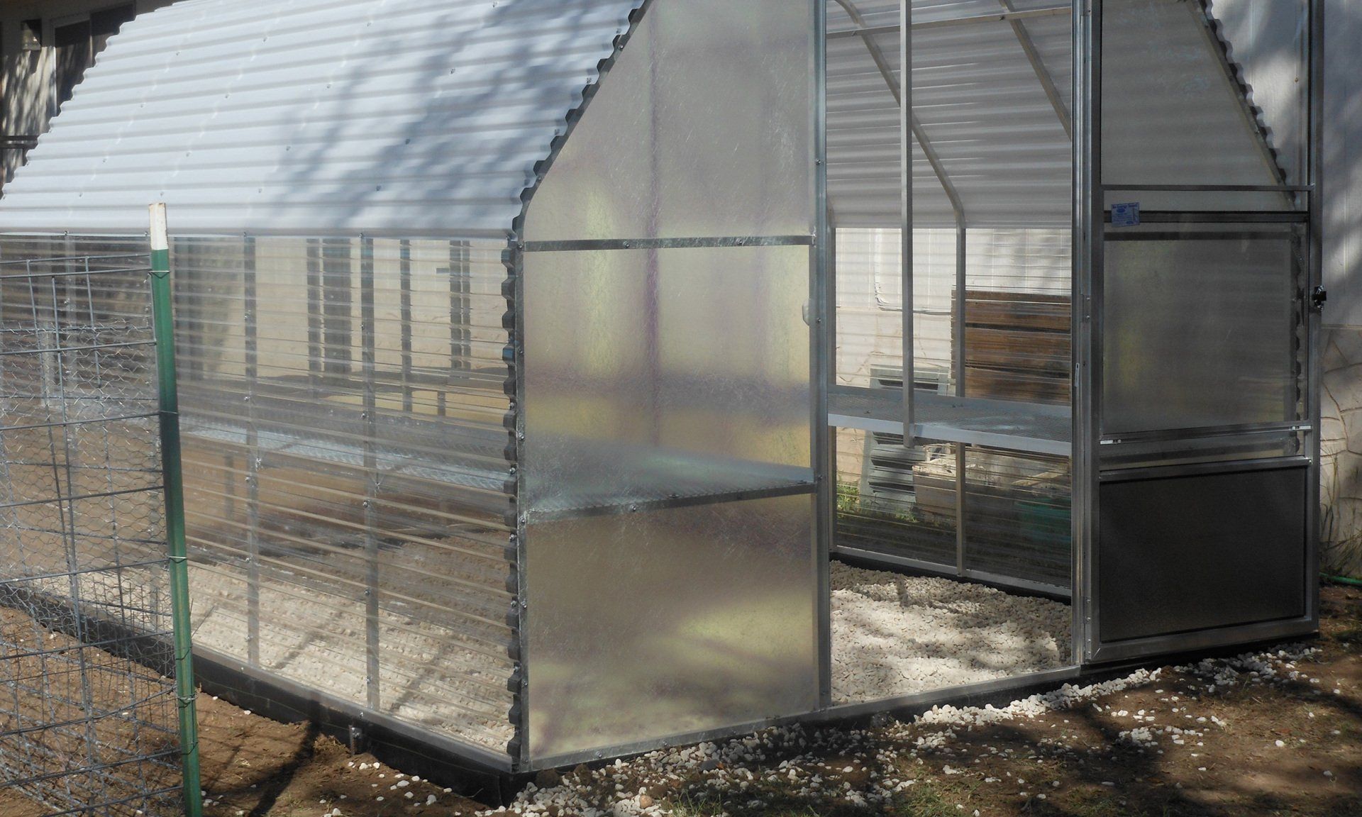 A greenhouse is sitting in the dirt next to a fence.