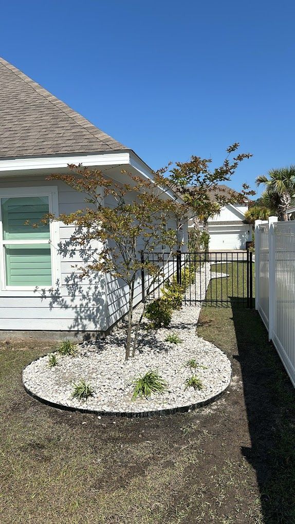 A small garden in front of a house with a tree in it.