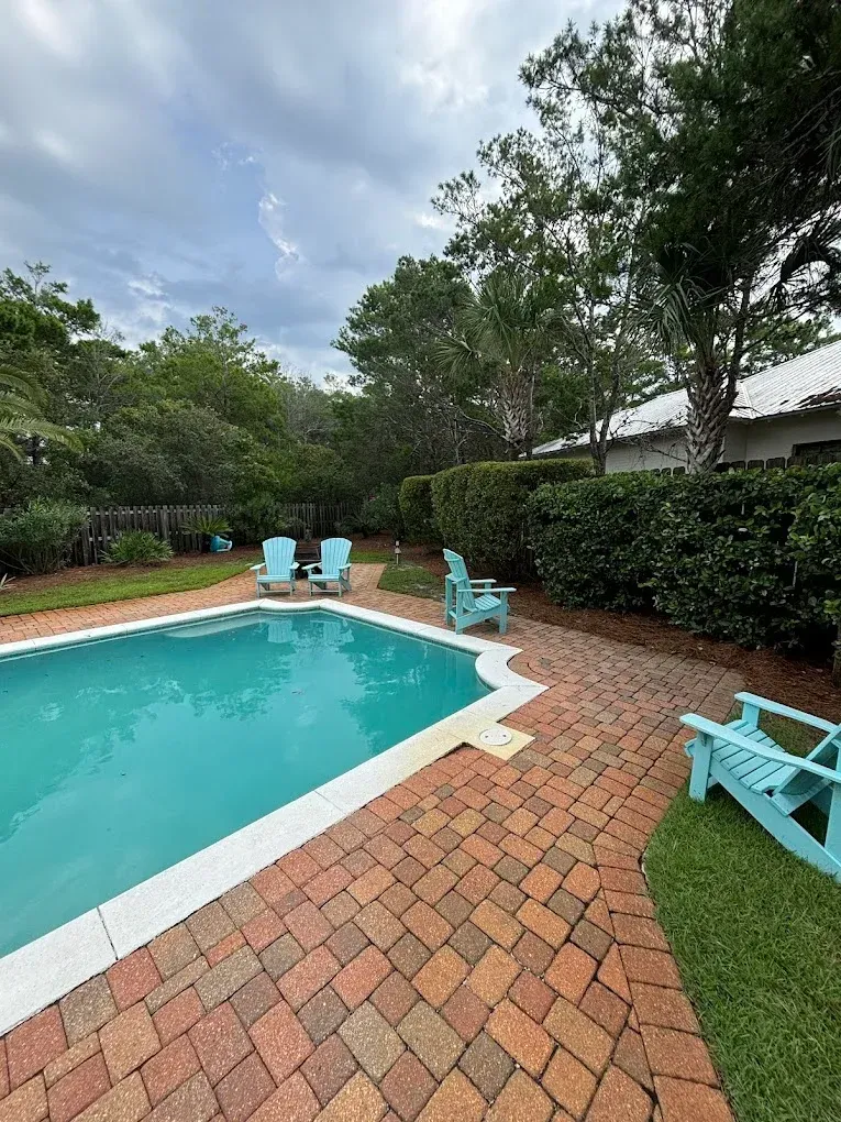 A large swimming pool surrounded by chairs and trees in a backyard.