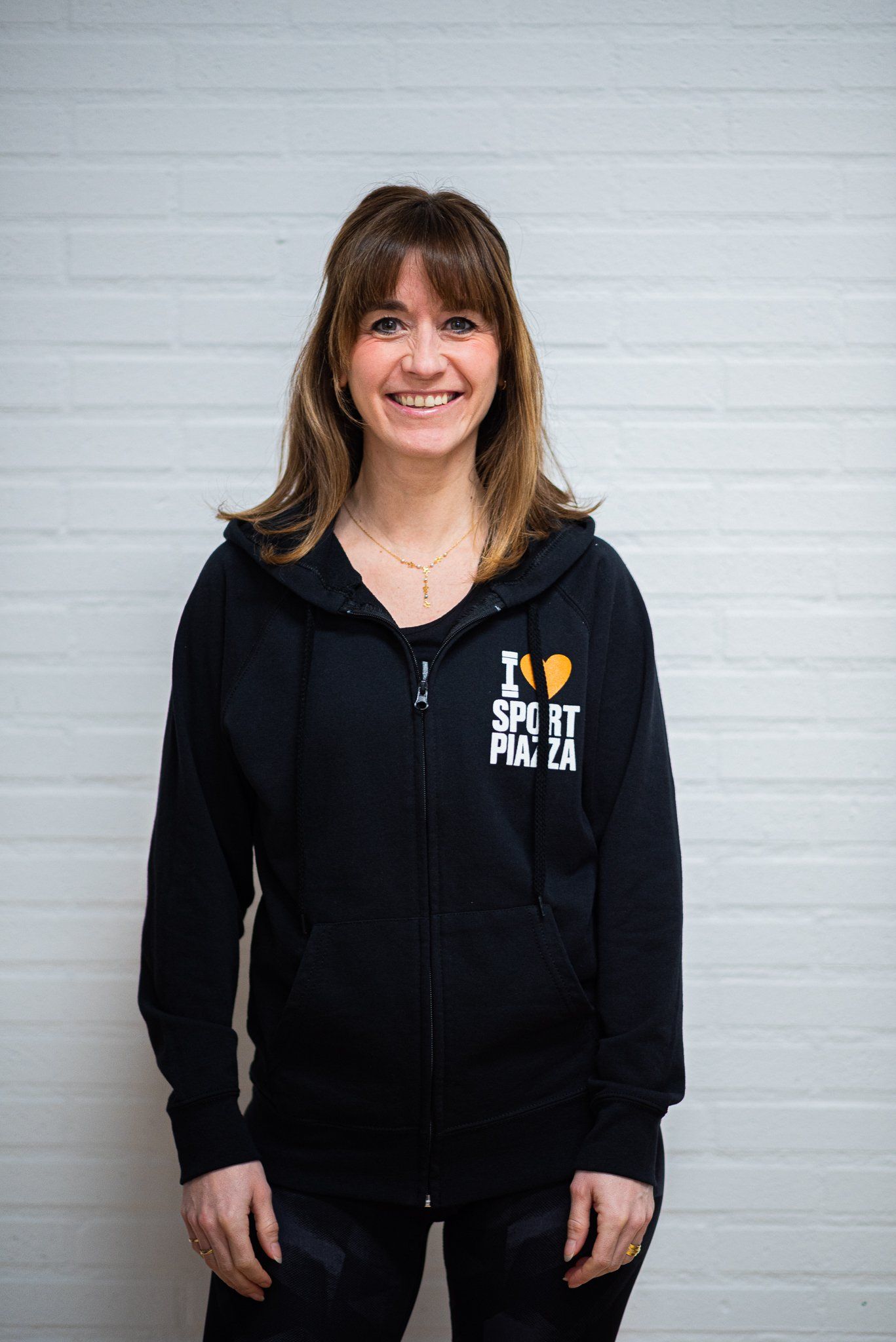 Een vrouw met een zwarte hoodie staat voor een witte muur.