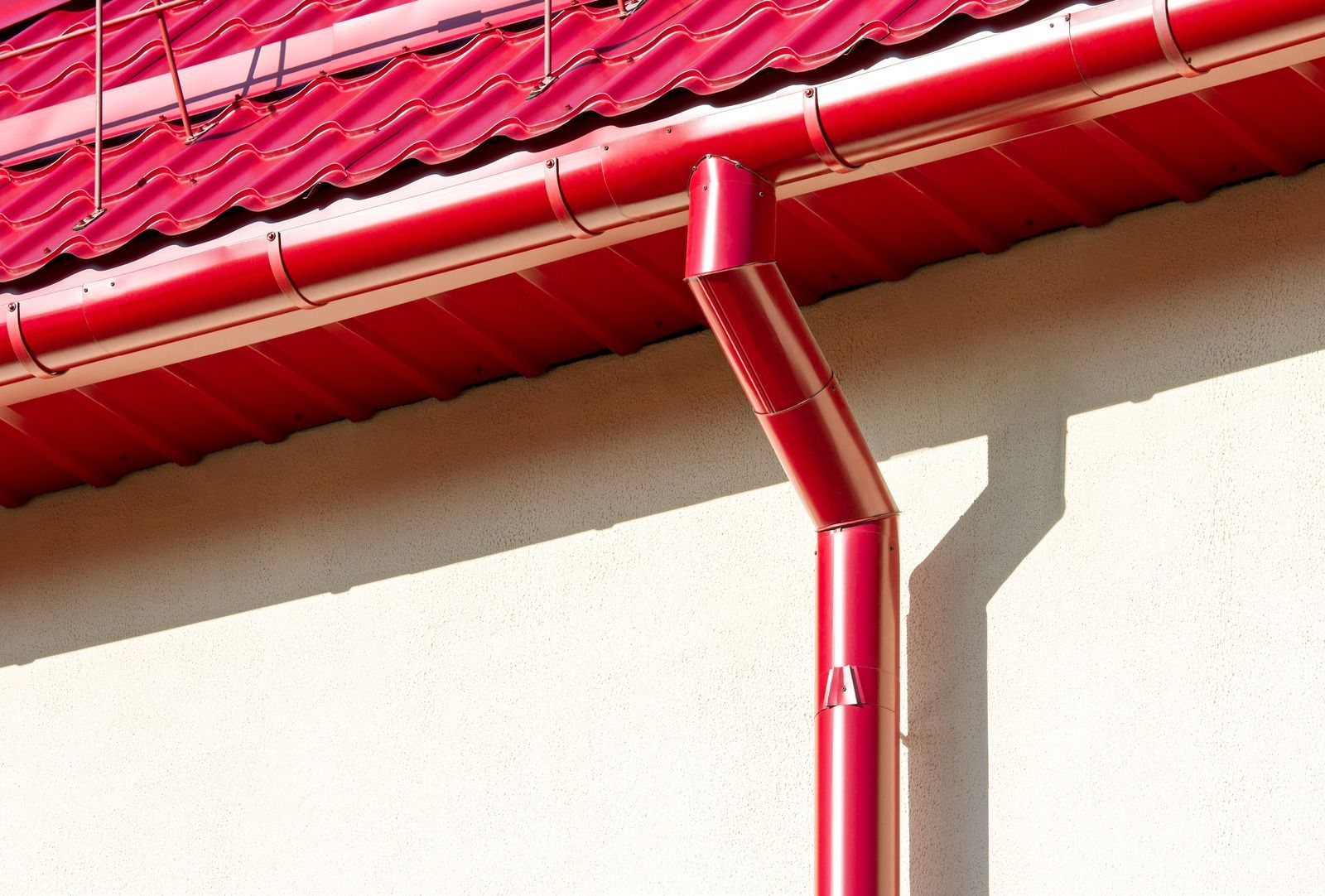 A red gutter on the side of a building with a red roof