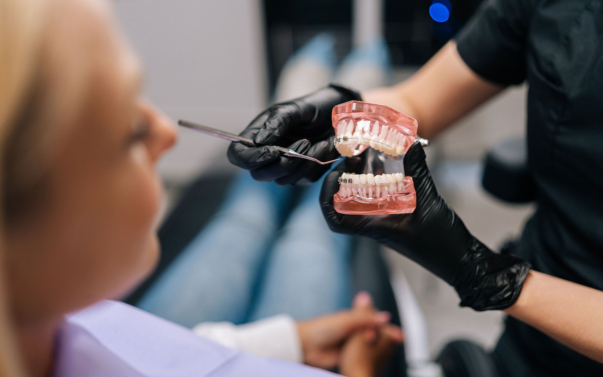 Dentist showing a dental model to a patient in a clinic; black gloves, pink gums, clear teeth.