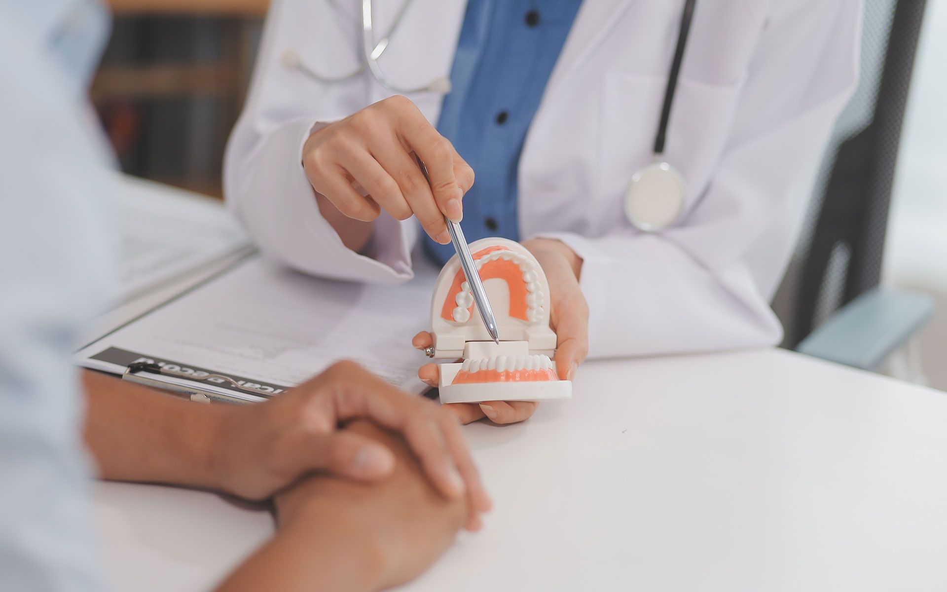 Doctor pointing at teeth model, explaining to a patient in an office setting.