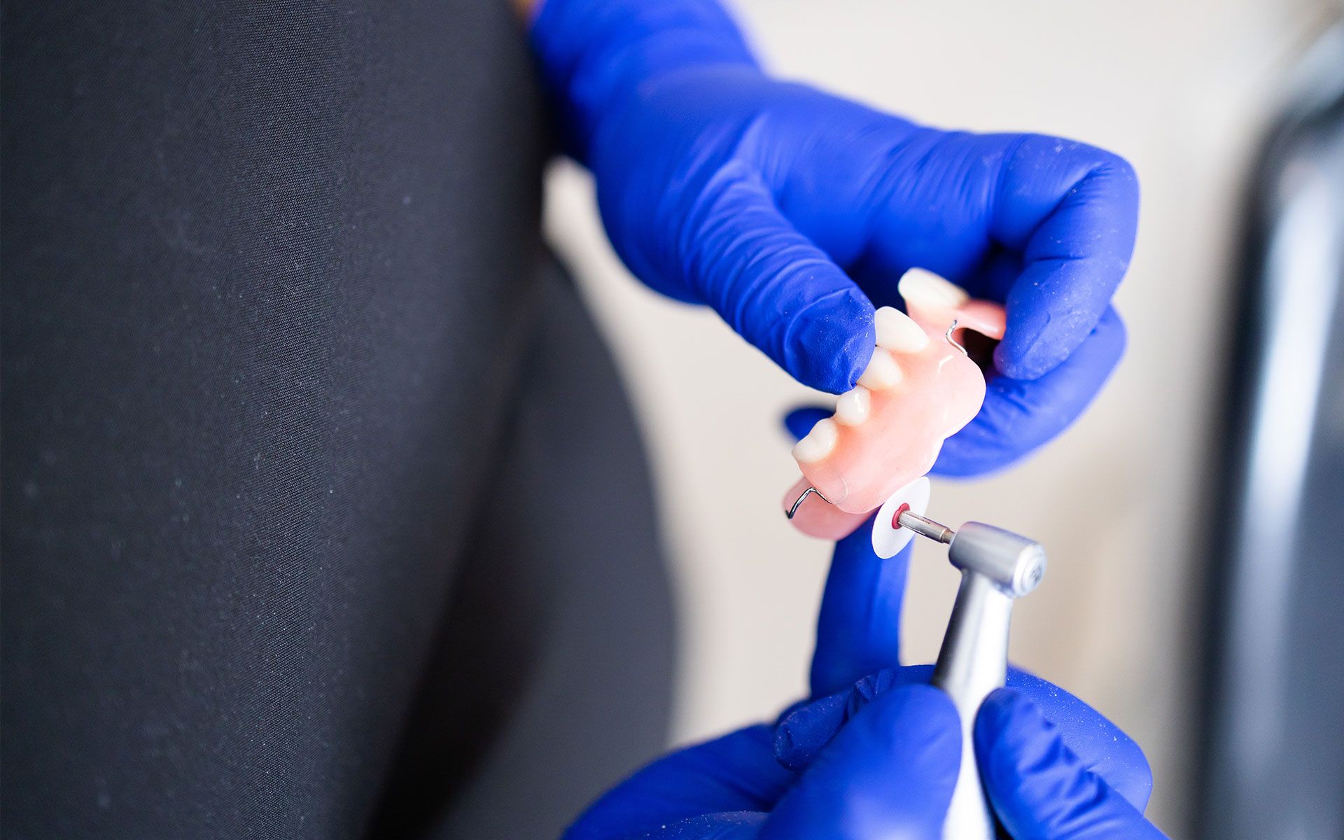 Person in blue gloves holding dentures and dental drill.